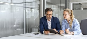 Zwei Personen betrachten im Büro gemeinsam ein Tablet und Unterlagen
